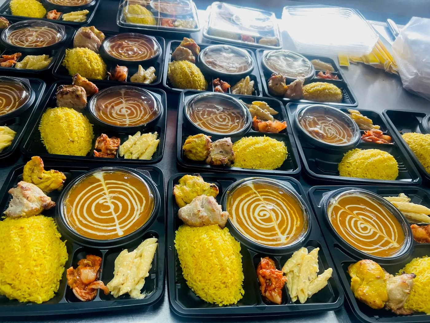 Rows of prepared boxed meals with saffron rice, curry and tandoori chicken